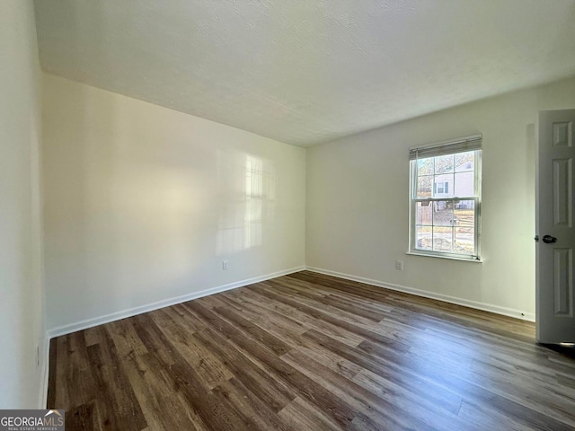 spare room featuring dark wood-style floors and baseboards