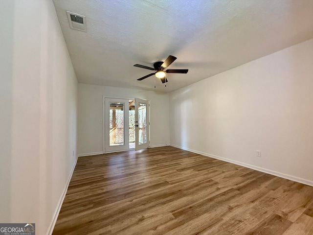 empty room with visible vents, a ceiling fan, a textured ceiling, wood finished floors, and baseboards