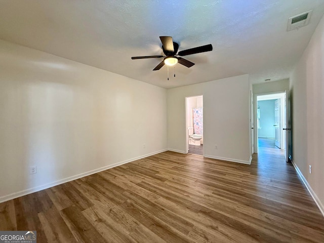 empty room featuring ceiling fan, a textured ceiling, dark wood-style flooring, visible vents, and baseboards