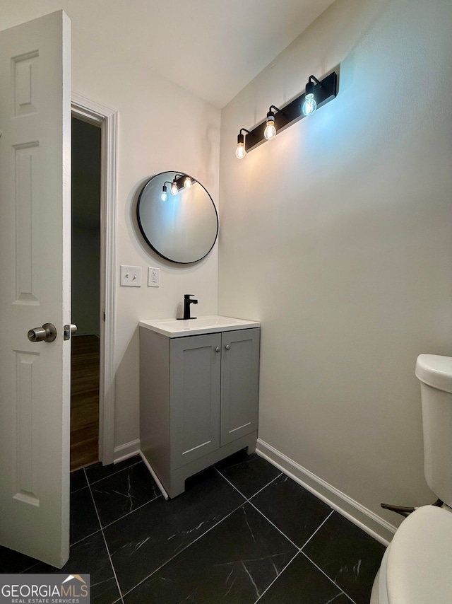 half bathroom featuring toilet, marble finish floor, baseboards, and vanity