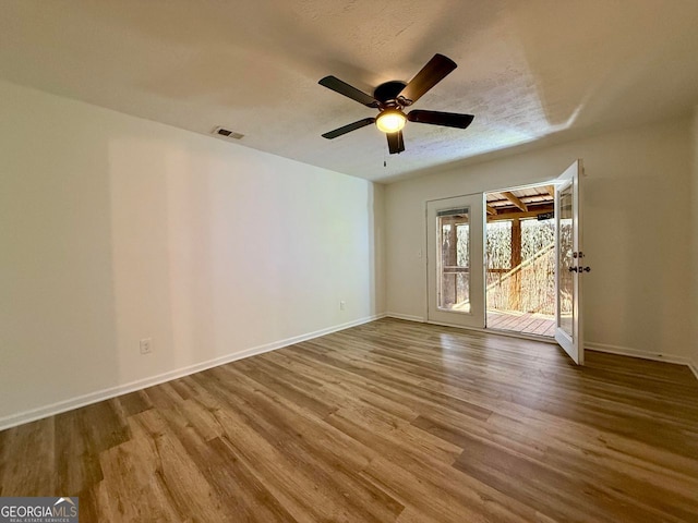 spare room with a textured ceiling, wood finished floors, a ceiling fan, visible vents, and baseboards