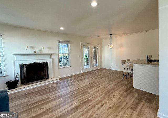 living area featuring french doors, recessed lighting, a fireplace with raised hearth, wood finished floors, and baseboards