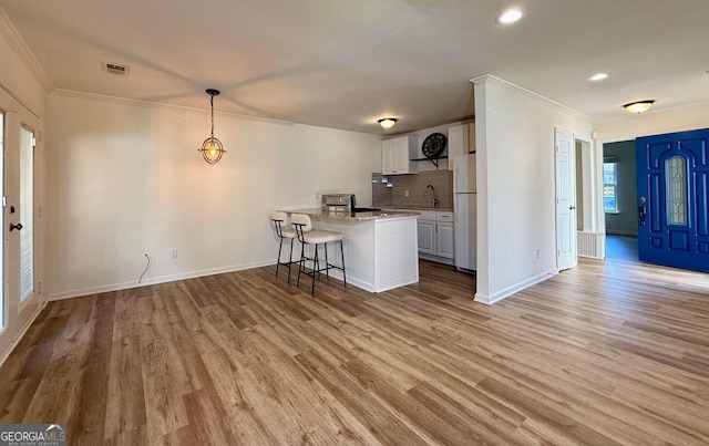 kitchen featuring visible vents, a breakfast bar area, freestanding refrigerator, and light wood-style floors