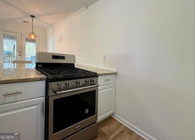 kitchen with stainless steel gas range oven, wood finished floors, white cabinetry, baseboards, and pendant lighting