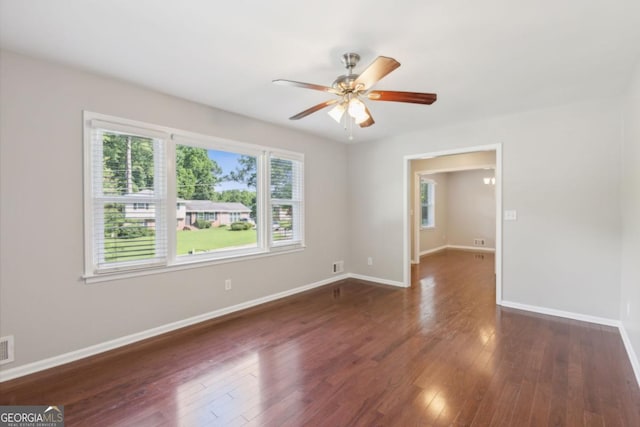 empty room featuring a ceiling fan, visible vents, baseboards, and wood finished floors