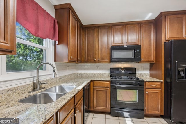 kitchen with a sink, backsplash, black appliances, and light stone countertops