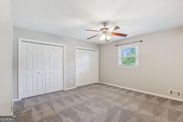 unfurnished bedroom featuring a ceiling fan, visible vents, baseboards, carpet, and two closets