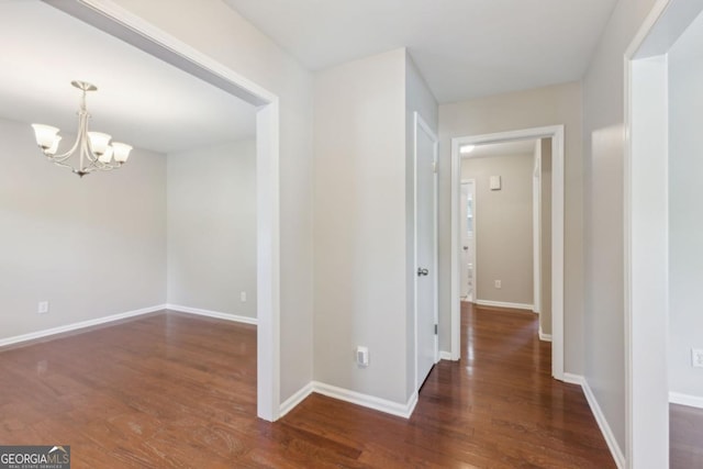 hallway with baseboards, an inviting chandelier, and wood finished floors