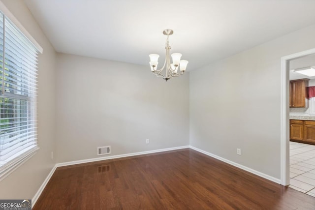 spare room with wood finished floors, visible vents, baseboards, and an inviting chandelier