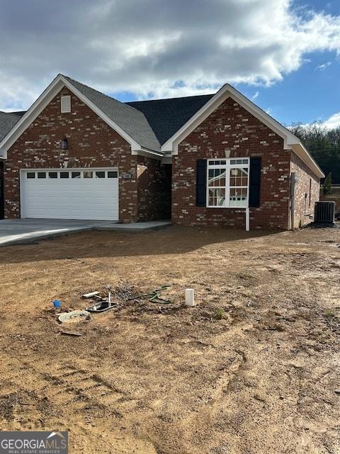 single story home with an attached garage, cooling unit, and brick siding