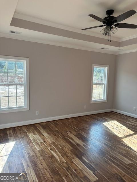 empty room with dark wood-style floors, ornamental molding, a raised ceiling, and visible vents