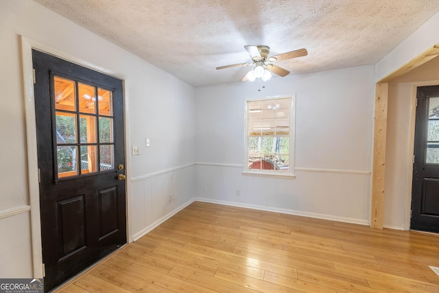 entryway featuring a textured ceiling, a wainscoted wall, a ceiling fan, and light wood-style floors