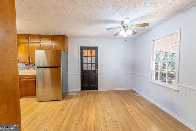 kitchen featuring a textured ceiling, visible vents, light wood-style floors, freestanding refrigerator, and brown cabinets