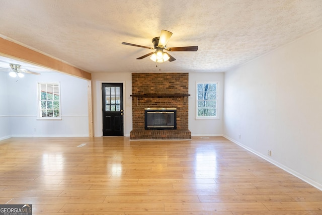 unfurnished living room with a brick fireplace, a healthy amount of sunlight, ceiling fan, and light wood-style flooring