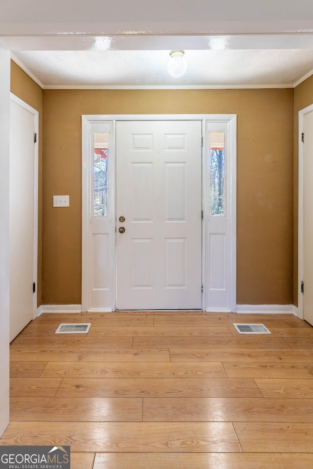 entryway featuring light wood finished floors, visible vents, and ornamental molding