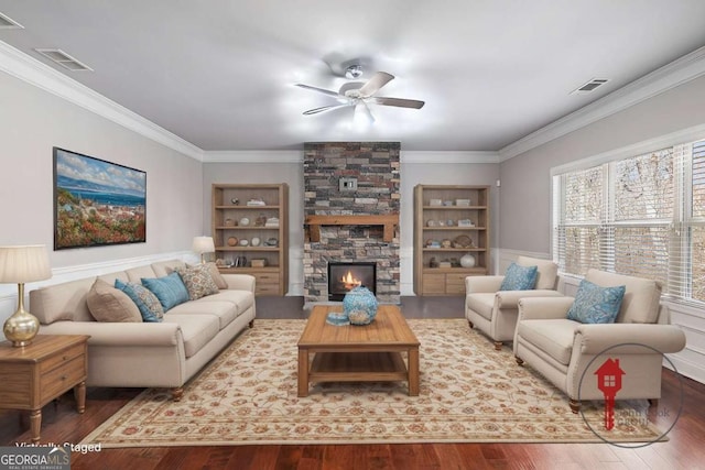 living area featuring a stone fireplace, wood finished floors, visible vents, and crown molding