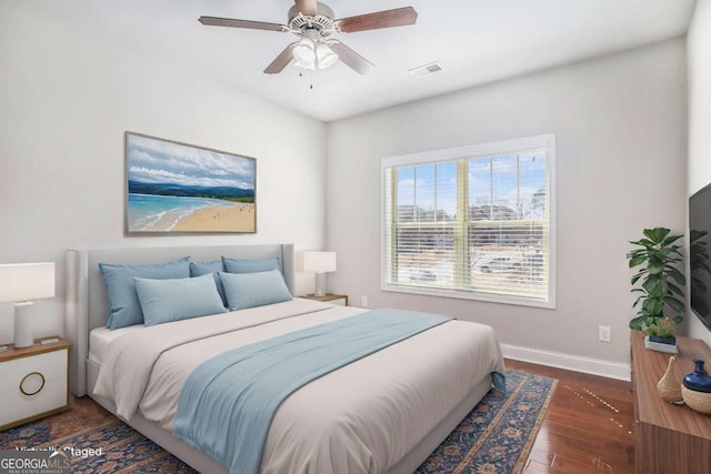 bedroom with a ceiling fan, visible vents, baseboards, and wood finished floors