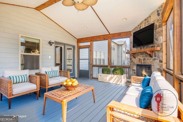 sunroom / solarium featuring lofted ceiling with beams, an outdoor stone fireplace, and a ceiling fan