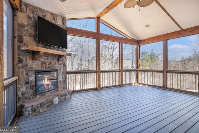 unfurnished sunroom featuring lofted ceiling with beams, a stone fireplace, and a ceiling fan