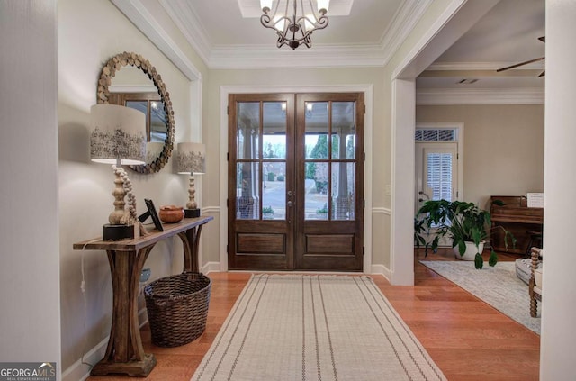 entryway with crown molding, a chandelier, wood finished floors, and french doors