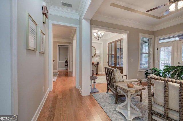 corridor featuring baseboards, visible vents, crown molding, light wood-style floors, and a notable chandelier