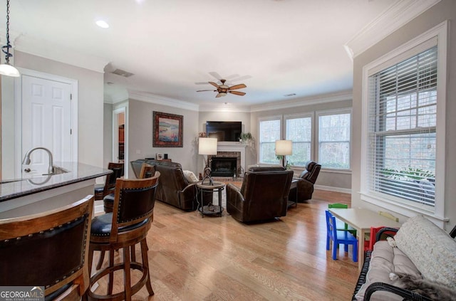 living area with light wood finished floors, ornamental molding, a ceiling fan, a brick fireplace, and baseboards