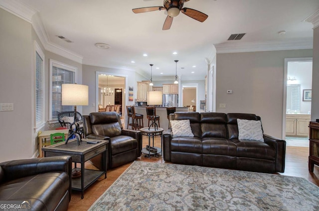 living area featuring ceiling fan with notable chandelier, ornamental molding, visible vents, and recessed lighting