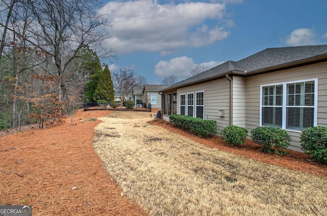 view of property exterior with a shingled roof and a lawn