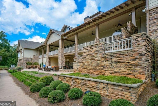 exterior space featuring a ceiling fan, a balcony, stone siding, a chimney, and a patio area