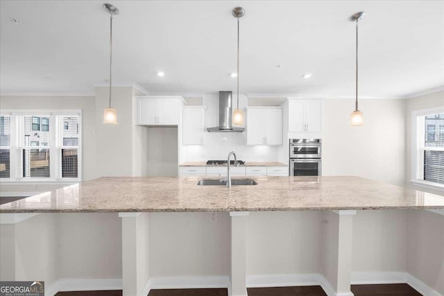 kitchen featuring appliances with stainless steel finishes, a large island with sink, wall chimney range hood, white cabinetry, and a sink