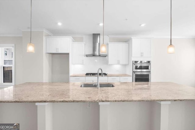 kitchen with wall chimney exhaust hood, appliances with stainless steel finishes, a large island with sink, white cabinetry, and a sink