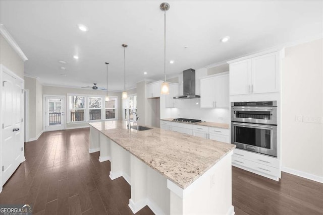 kitchen featuring stainless steel double oven, white cabinets, a sink, and wall chimney range hood