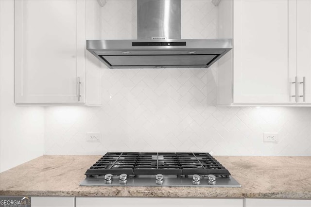 kitchen featuring stainless steel gas cooktop, light stone counters, wall chimney range hood, white cabinetry, and backsplash