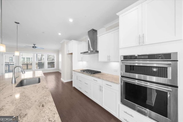 kitchen with light stone counters, stainless steel appliances, white cabinetry, a sink, and wall chimney exhaust hood