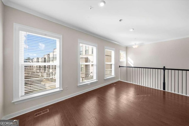 empty room with baseboards, visible vents, wood finished floors, and ornamental molding