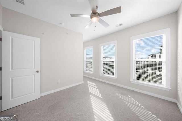 carpeted spare room with visible vents, ceiling fan, and baseboards