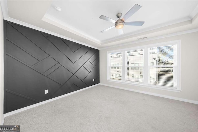 spare room featuring carpet floors, a raised ceiling, and baseboards