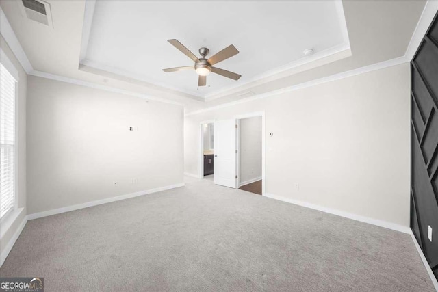 unfurnished bedroom featuring carpet floors, visible vents, baseboards, a raised ceiling, and crown molding