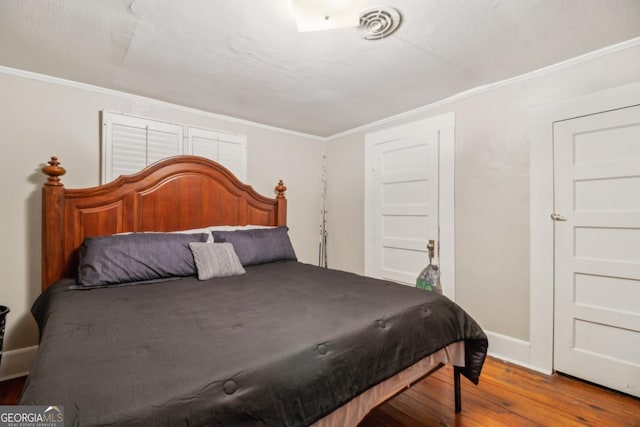 bedroom featuring baseboards, crown molding, visible vents, and wood finished floors