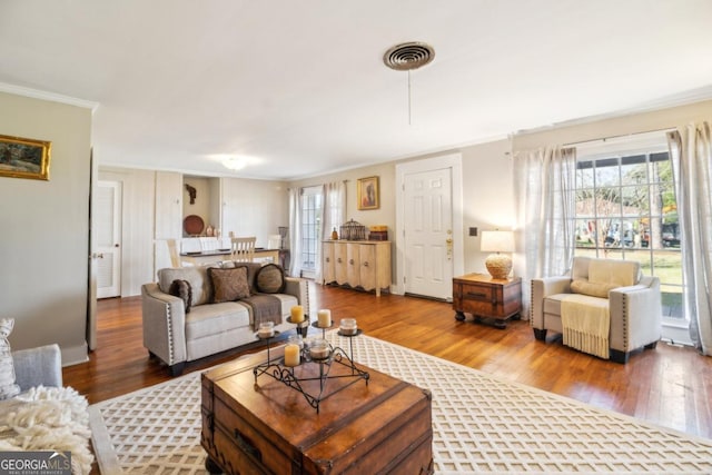 living area with visible vents, wood finished floors, and ornamental molding