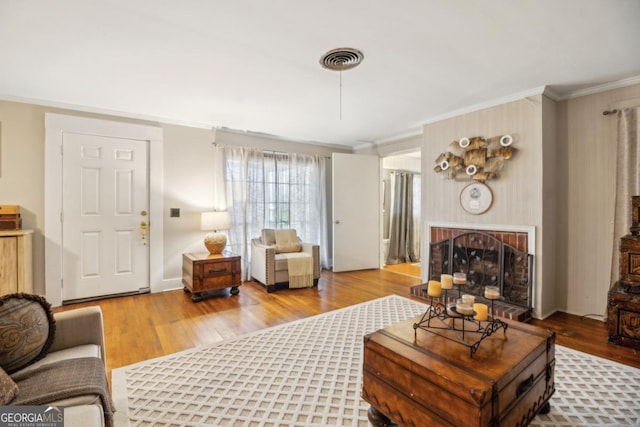 living room with a fireplace, wood finished floors, visible vents, baseboards, and crown molding