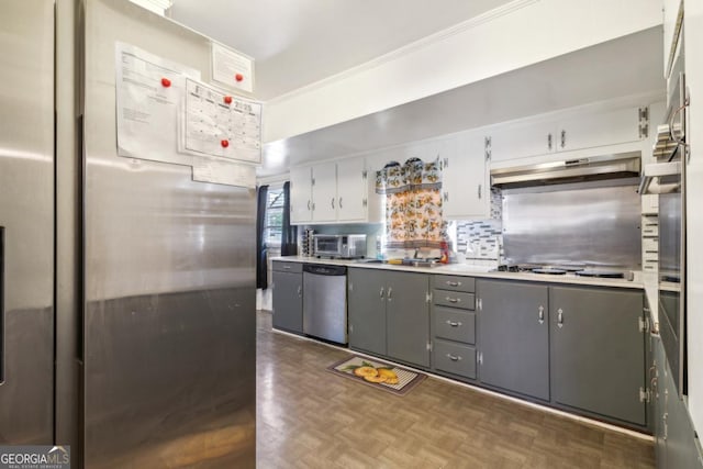 kitchen with gray cabinetry, under cabinet range hood, light countertops, appliances with stainless steel finishes, and decorative backsplash