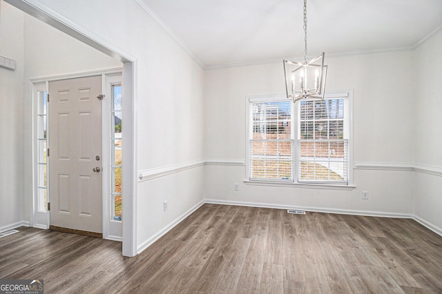 unfurnished dining area featuring crown molding, visible vents, an inviting chandelier, wood finished floors, and baseboards