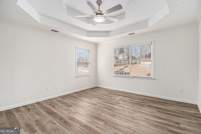 empty room featuring baseboards, visible vents, a raised ceiling, and wood finished floors