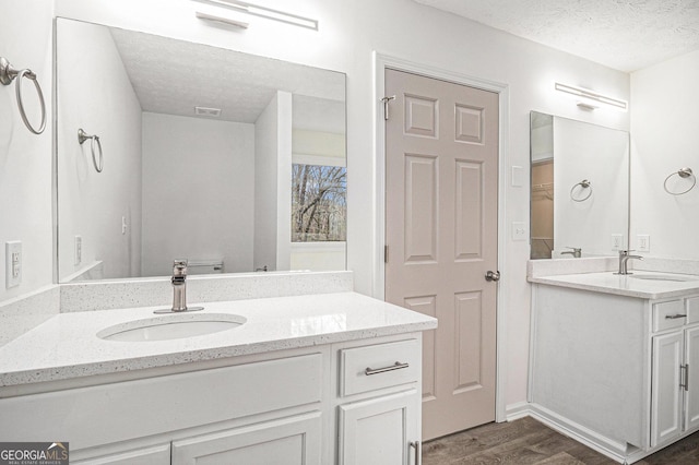 bathroom with a textured ceiling, wood finished floors, two vanities, and a sink