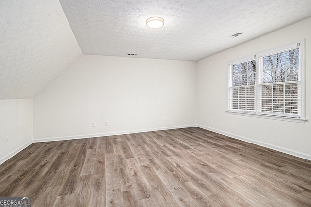 bonus room featuring baseboards, visible vents, vaulted ceiling, and wood finished floors