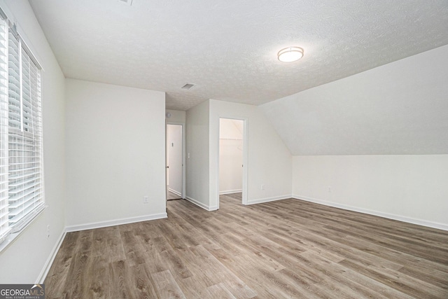 additional living space featuring lofted ceiling, a textured ceiling, baseboards, and wood finished floors