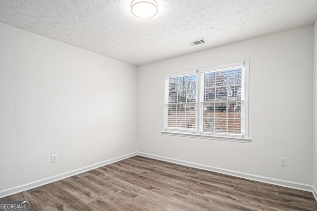 empty room with a textured ceiling, dark wood-style flooring, visible vents, and baseboards