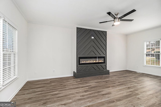 unfurnished living room featuring a large fireplace, ornamental molding, wood finished floors, and baseboards