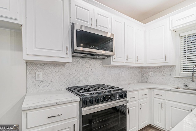 kitchen with appliances with stainless steel finishes, white cabinets, a sink, and backsplash